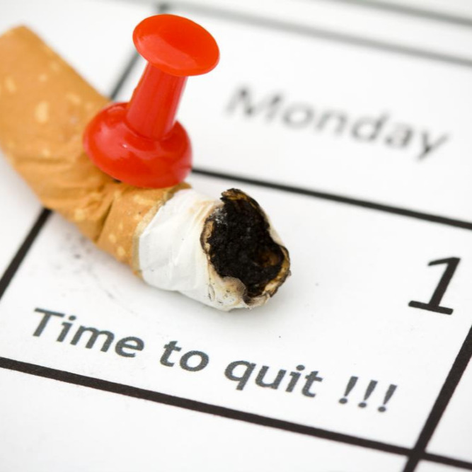 A pushpin pushed through the butt of a cigarette on a calendar with the words, "Time to quit!" written.