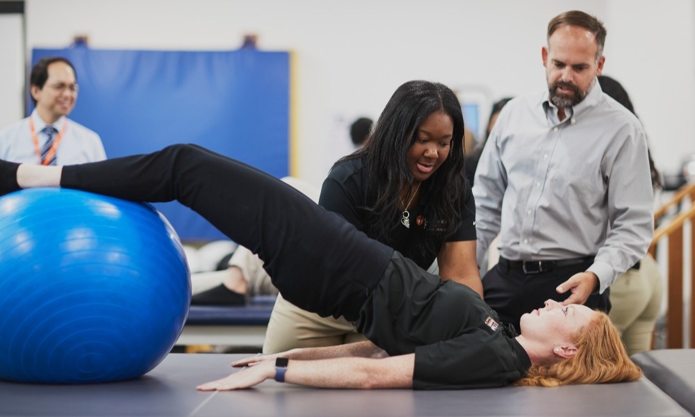 Physical therapy doctoral students practice exercises with yoga ball while professor watches