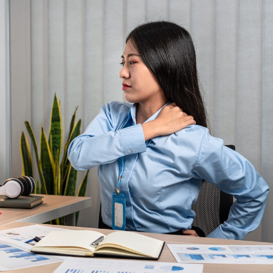 Woman at her desk holding her shoulder in pain.