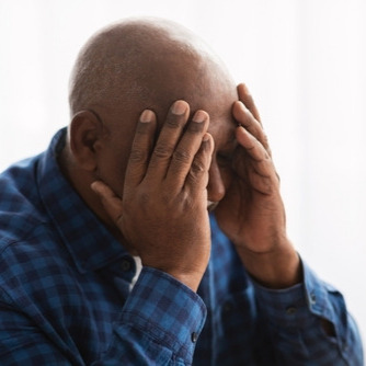 Older Black man holds his head in his hands.